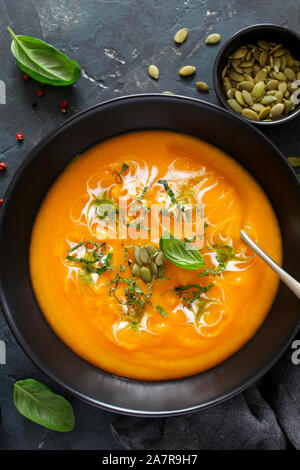 Kürbis und Karotten Suppe mit Sahne und Basilikum auf dunklem Hintergrund. Ansicht von oben mit der Kopie. Stockfoto