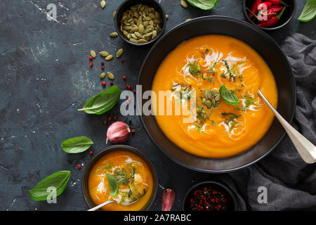 Kürbis und Karotten Suppe mit Sahne und Basilikum auf dunklem Hintergrund. Ansicht von oben mit der Kopie. Stockfoto