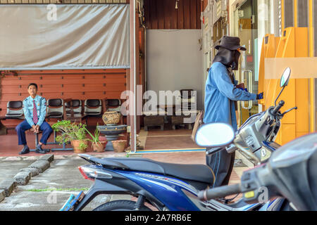 Khao Lak, Thailand, 30. August 2019: ein Mann mit Hut und ein bandana Maske, die aussehen wie ein Bandit oder ein Verbrecher in der Nähe von einem gelben ATM. Die Bank Guard ist Stockfoto