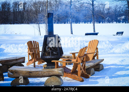 Holzbänke und Stühle mit Kamin mit Brennholz in den Rastplatz während der Wintersaison. Holz - brennende Feuergrube mit abnehmbaren Feuer p Stockfoto
