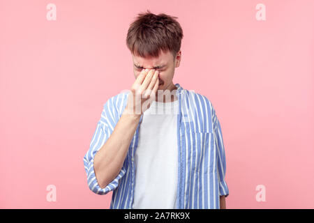 Portrait von frustriert Junge braunhaarige Mann in casual Striped Shirt berühren geschlossenen Augen, Weinen von Depressionen, Trauer oder Schmerz, hoffnungslos. Ich Stockfoto