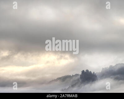 Bewölkt, hügeligen Landschaft. Blick über schwere Wolke in der felsigen Schlucht voll mit tiefen Wald. Sonne in den Wolken versteckt. Stockfoto