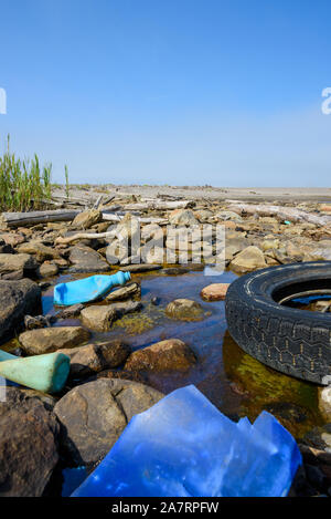 Auto Reifen- und Plastikflaschen in schlammigen Pfütze auf Strand. Ozean Kunststoff Umweltverschmutzung. Stockfoto
