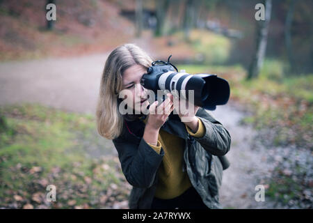 Blond Fotograf hocken und die Verwendung einer Kamera mit grossem Teleobjektiv während der Aufnahmen in der Natur Stockfoto