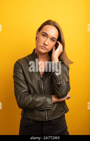 Porträt einer jungen Frau trug eine Lederjacke vor gelbem Hintergrund Stockfoto