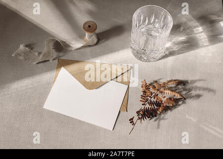 Herbst, Herbst Schreibwaren mockup Szene. Leere Grußkarte, Einladung, Handwerk Papier Umschlag, chemische Farn Blatt und funkelnde Glas Wasser auf Graue Tabelle Stockfoto