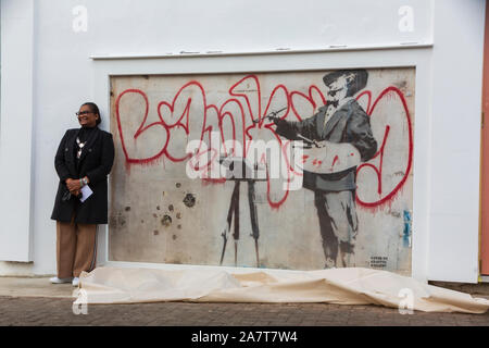 London, Großbritannien. 4. Okt 2019. Neu Banksy Kunstwerk 'Graffiti Maler' offenbart durch Royal Borough von Kensington und Chelsea Stellvertretender Bürgermeister Cllr Walaa Idris, und Enstar capital CEO Simon Lyons in London Notting Hill wiederhergestellt. Die banksy Artwork wiederhergestellt durch Enstar wird auf permanente Anzeige für die Gemeinschaft bleiben. An der Ecke der Ackam Straße und der Portobello Road, dem Stencil Artwork "Graffiti Maler' stellt Spanischen Barock Maler Diego Velasquez Gemälde "BANKSY" in roter Farbe auf einer weißen Giebelwand. Credit: thamesfleet/Alamy leben Nachrichten Stockfoto