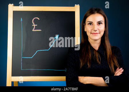 Pound Pfeil Chart des Wachstums ist auf einem schwarzen Kreidetafel, eine glückliche Frau, die in der Nähe stehenden wird gezeichnet Stockfoto