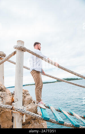 Man Walking durch touristische Suspension Bridge crossing Sea Bay Stockfoto