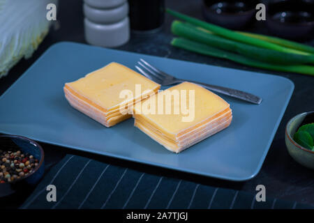 Zwei Heftklammern von Scheiben Käse mit der Bezeichnung "Raclette", in der Regel für das Schmelzen für Schweizer Gericht verwendet, auf eine graue Platte Stockfoto