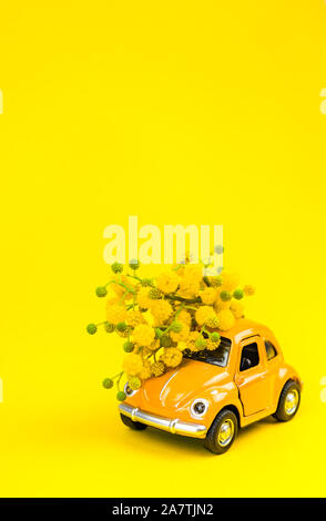 Moskau, Russland - 23. Februar, 8. März 2019: Internationaler Tag der Frau Karte mit Spielzeug Modell der retro Auto Lieferung Blumenstrauß von Mimosa Blumen auf Gelb Stockfoto