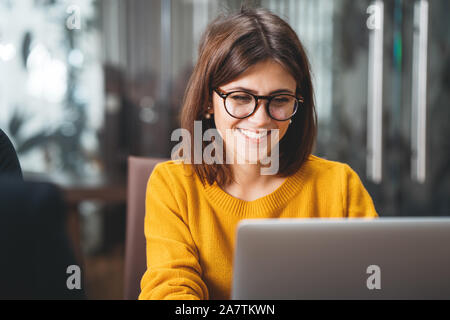 Portrait von Happy business Frau mit Brille am Arbeitsplatz im Büro. Junge schöne Arbeiterin mit modernen Laptop Stockfoto