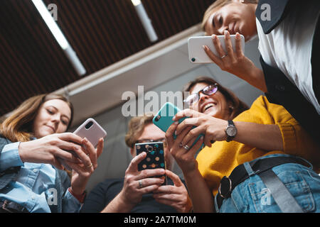 Gruppe von positiven Menschen zusammen zu arbeiten und durch den Einsatz von modernen Smartphone im Büro. Digitale gadgets mit Konzept Stockfoto