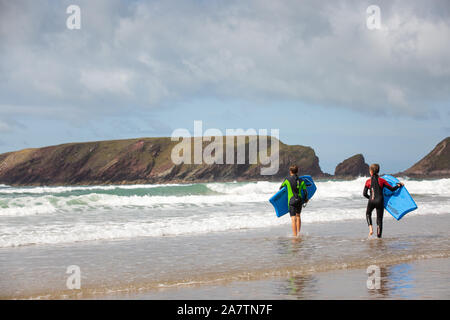 Zwei Jungen tragen ihre Surfbretter in am Meer an einem Strand in Pembrokeshire. Stockfoto