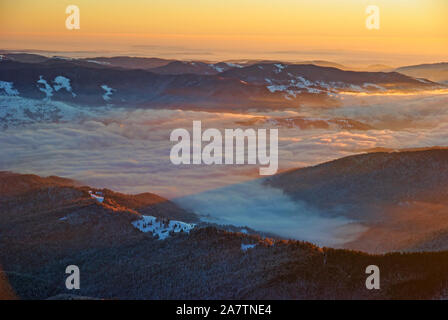 Winter Sonnenaufgang Panorama vom Gipfel in den rumänischen Karpaten, nebligen Tal und Sonnenstrahlen. Stockfoto