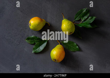 Drei reife, gelbe, grüne und rote Birnen auf einem grauen Tisch liegen. Blick von oben. Stockfoto