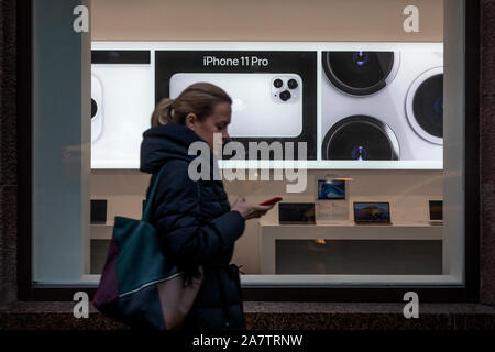 Moskau, Russland. November, 2019 ein Mädchen geht auf der Straße mit einem Mobiltelefon, das auf dem Hintergrund einer Werbung für das Iphone 11 Pro Telefon in einem Apple Store auf der Tverskaya Straße in Moskau, Russland Stockfoto