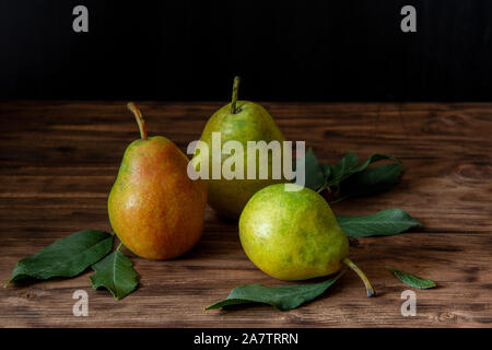 Drei reife, gelbe, grüne und rote Birnen auf einem hölzernen Tisch liegen. Stockfoto