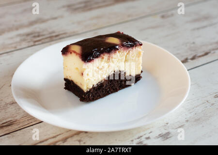 Ein Stück Käsekuchen mit fruchtiger Marmelade auf der Oberseite. Ein Stück Schokoladenkuchen mit Sahne und Frischkäse auf weiße Platte. Stockfoto