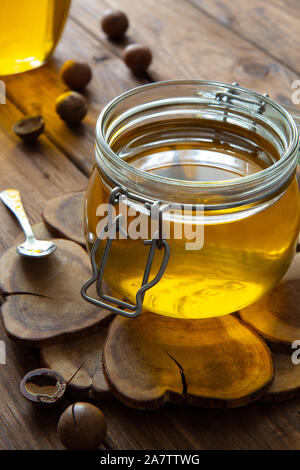 Ghee oder Butterschmalz in einem Glas auf einem Stand aus Holz auf einem Holztisch. Die Zusammensetzung wird durch einen kleinen Löffel und Macadamianüsse ergänzt. Stockfoto