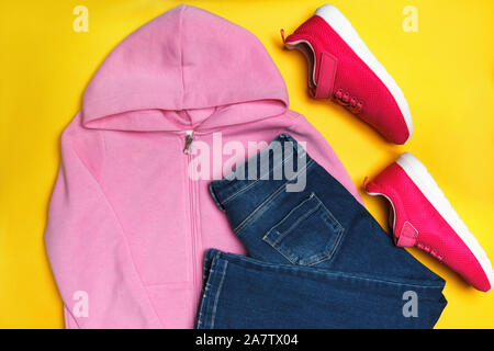 Blick von oben auf eine Komposition von legere Kleidung für ein Mädchen auf einem gelben Hintergrund. Sweatshirt, Jeans, Turnschuhe. Stockfoto