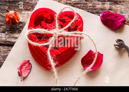 Gemusterte Herz gebunden mit einem Seil unter trockenen Rosenblüten Stockfoto