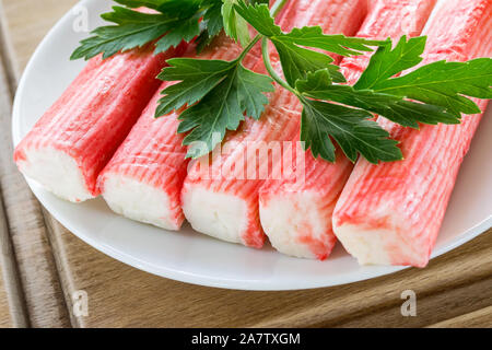 Reihe von Surimi Crab Sticks und Petersilie auf einem weißen Untertasse über ein braunes Holz Schneidebrett. Meeresfrüchte und Zutat für Salate. Das gesunde Essen. Close-up Stockfoto