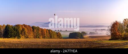 Nebligen Herbstmorgen im Böhmischen Paradies. Die Ruine der Burg Trosky und den Heißluftballon im Hintergrund. Stockfoto