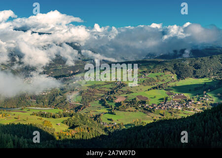 Blick von einem Berg auf das Dorf Ums, Voels am Schlern, in den italienischen Alpen an einem sonnigen Tag mit dichten weißen Wolken über blühende Stockfoto