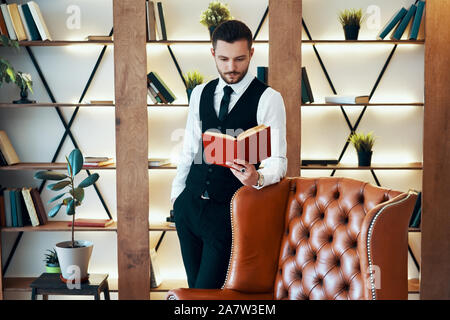 Hübscher junger Mann im eleganten Anzug mit einem Buch in einen modernen, luxuriösen Interieur. Hobby Konzept Stockfoto