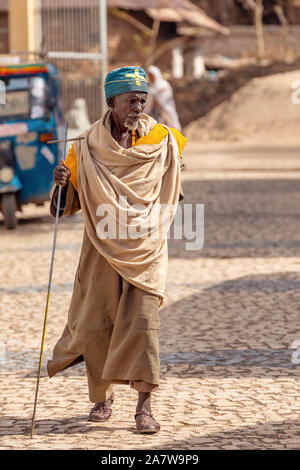 AXUM, Äthiopien, 27. APRIL 2019: Alter Mann, orthodoxen Mönch oder Priester Spaziergang mit krücke auf leere Straße von Aksum am 27. April 2019 in Aksum, Äthiopien Afric Stockfoto