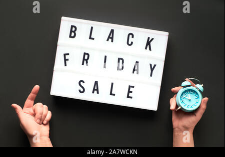Lightbox Text 'Black Friday Sale" auf schwarzem Papier Hintergrund. Kreative flach mit zwei Händen, einer Holding Wecker und ein weiterer Hinweis auf die Tex Stockfoto
