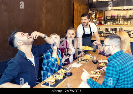 Gruppe der besten Freunde essen lecker Essen im kleinen Restaurant während der glückliche Besitzer ihnen gedient haben junge Menschen die Zeit zusammen genießen im trendigen Pub Stockfoto