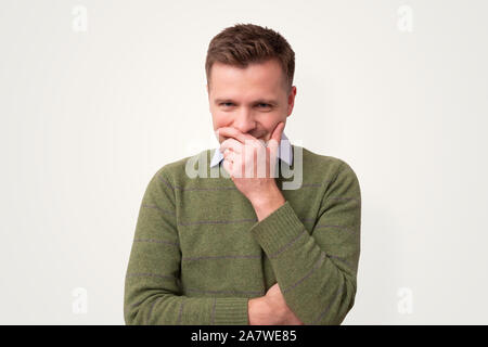 Schüchtern kaukasischen Mann kichert über den Mund mit der Hand. Studio shot Stockfoto