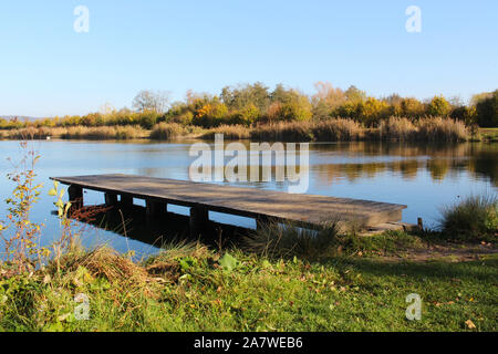 Hölzerne Seebrücke an einem See mit reflektierenden Küste im Hintergrund Stockfoto