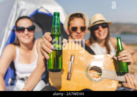 Gitarre Spieler mit Flasche Bier, während eine große Zeit mit seinen Freunden beim Camping am Strand. Stockfoto