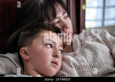 Asiatische vietnamesische Frau im Bett mit Ihrem gemischten Rennen asiatischen Kaukasischen Sohn starrte aus dem Fenster mit traurigem Ausdrücke Stockfoto