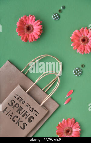 Coral Gerbera daisy flowers und Handwerk Papier Einkaufstüten auf grünem Papier Hintergrund, Null Abfall umweltfreundlich lebendiges Konzept. Text "Null Abfall Feder h Stockfoto