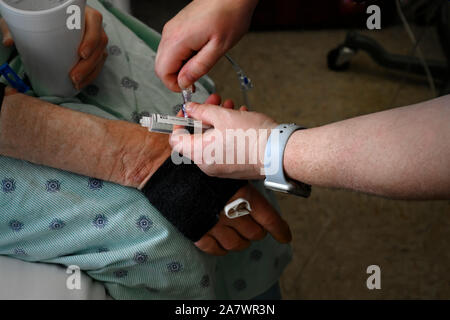 Nahaufnahme einer Krankenschwester Einfügen einer Kochsalzlösung Spritze in den Arm eines älteren männlichen Patienten. Stockfoto