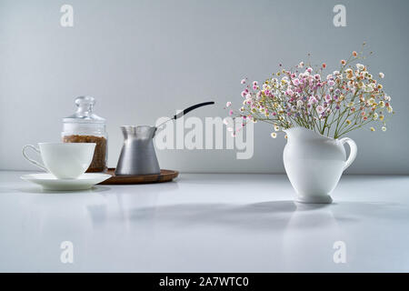 Zusammensetzung mit weißem Porzellan Tee-ware auf einem hellgrauen Hintergrund mit einem zarten Blumenstrauß Stockfoto