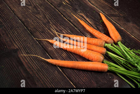 Bündel frische Karotte Wurzeln mit grünen Blättern auf dunklen alten hölzernen Board Stockfoto