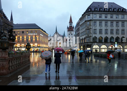 München. Bayern/Deutschland - April, 29 2019: Menschen unter Sonnenschirmen auf dem Marienplatz in München am regnerischen Abend Stockfoto