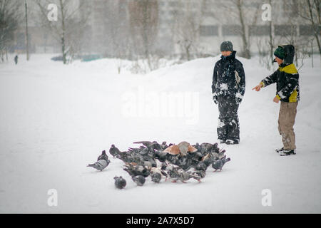 Zwei Jungen, die im Winter warme Kleidung füttert Tauben im City Park. Tauben im Schnee. Rescue Vögel im Winter von Hunger. Pflege für wilde Tiere. Stockfoto