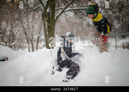 Zwei Jungen spielen auf Haufen Schnee nach starker Schneefall in der Stadt. Kinder, die auf einem Spaziergang im Park im Winter. Aktiv gesund Lifestyle. Stockfoto