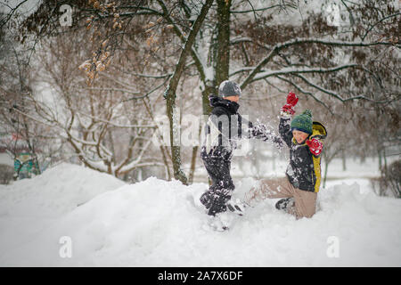 Zwei Jungen spielen auf Haufen Schnee nach starker Schneefall in der Stadt. Kinder, die auf einem Spaziergang im Park im Winter. Aktiv gesund Lifestyle. Stockfoto