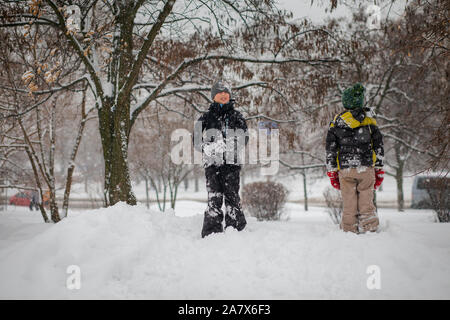 Zwei Jungen spielen auf Haufen Schnee nach starker Schneefall in der Stadt. Kinder, die auf einem Spaziergang im Park im Winter. Aktiv gesund Lifestyle. Stockfoto