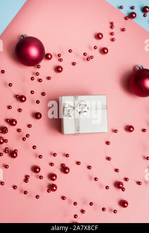 Silber kleines Geschenk auf Rosa und Blau pastell Hintergründe mit roten Weihnachtskugeln und Perlen. Das Konzept der, Geschenke, Überraschungen, Weihnachten, Neues Jahr. Stockfoto