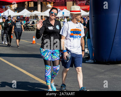 Farbenfroh gekleidete Frau ist winken und lächeln, wie Sie geht über die Ziellinie, während Sie die Hände mit ihren Mann auf der JDRF einen Spaziergang Fundraiser. Stockfoto