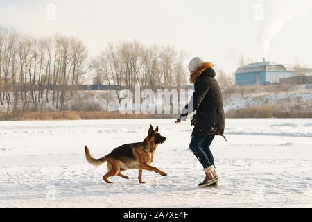 Stilvolle Kerl Spaziergang mit dem Hund. Spaß im Schnee spielen im Freien. Spielerische. Tierliebhaber. Deutscher Schäferhund genießen Sie die Freiheit. Freunde zusammen. Lustige e Stockfoto