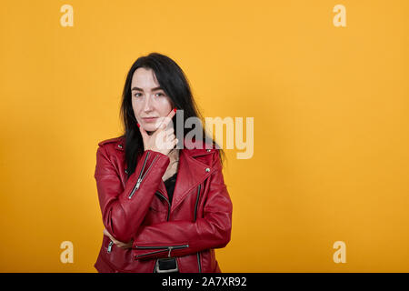 Junge Frau auf der Suche Kamera Hand am Kinn auf orange Hintergrund isoliert Stockfoto